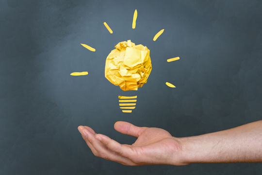 Symbolbild für Idee / Innovation: Foto einer geöffneten, nach oben zeigenden Hand, darüber Grafik einer leuchtenden Glühbirne 