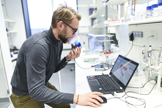 Mann mit Atemmaske vor Laptop in Laborumgebung